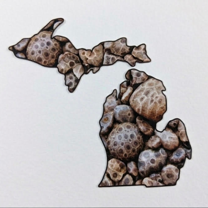 A decorative cutout or sticker in the shape of the state of Michigan, filled with a pattern of brown and beige Petosky stones, shown on a plain white background.